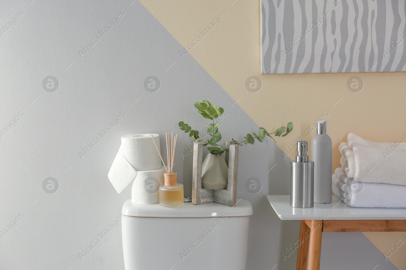 Photo of Table and toilet bowl with decor elements and necessities near color wall. Bathroom interior