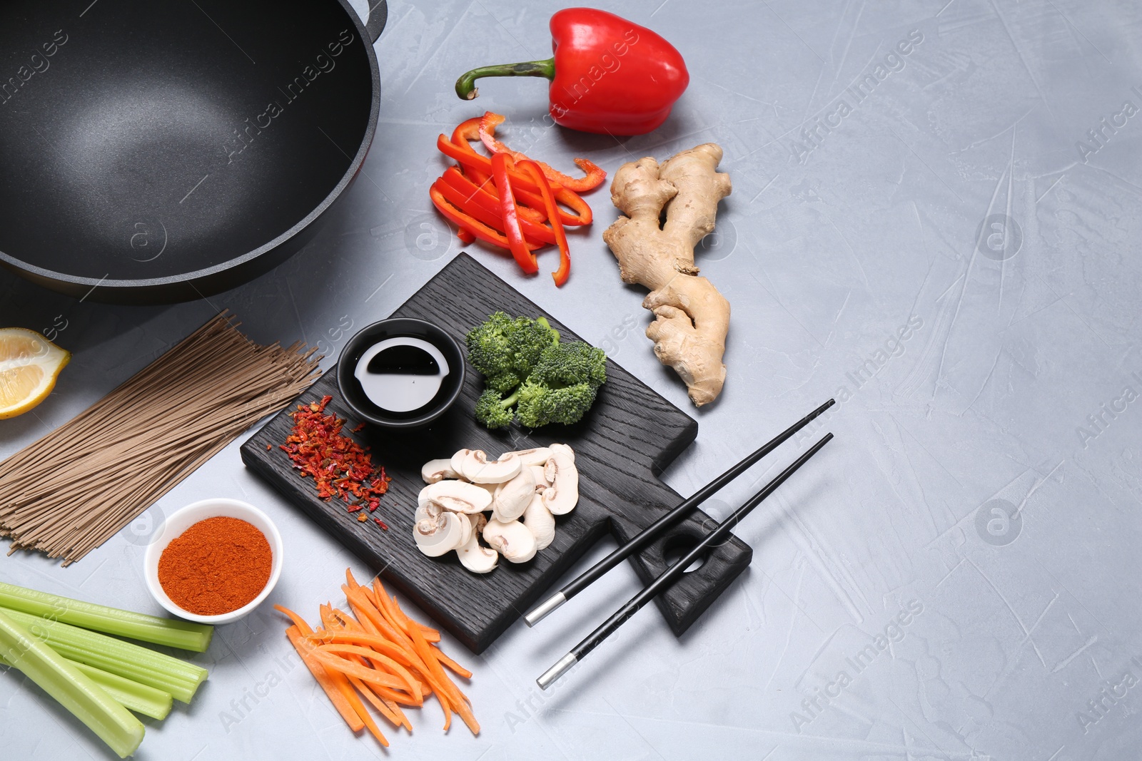 Photo of Wok, chopsticks and different products on grey table, space for text