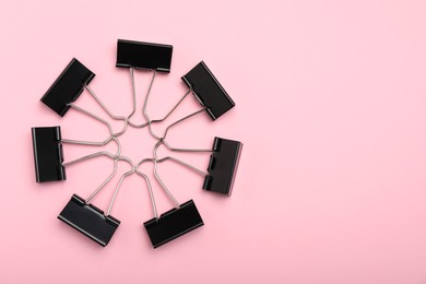 Photo of Black binder clips on pink background, flat lay. Space for text