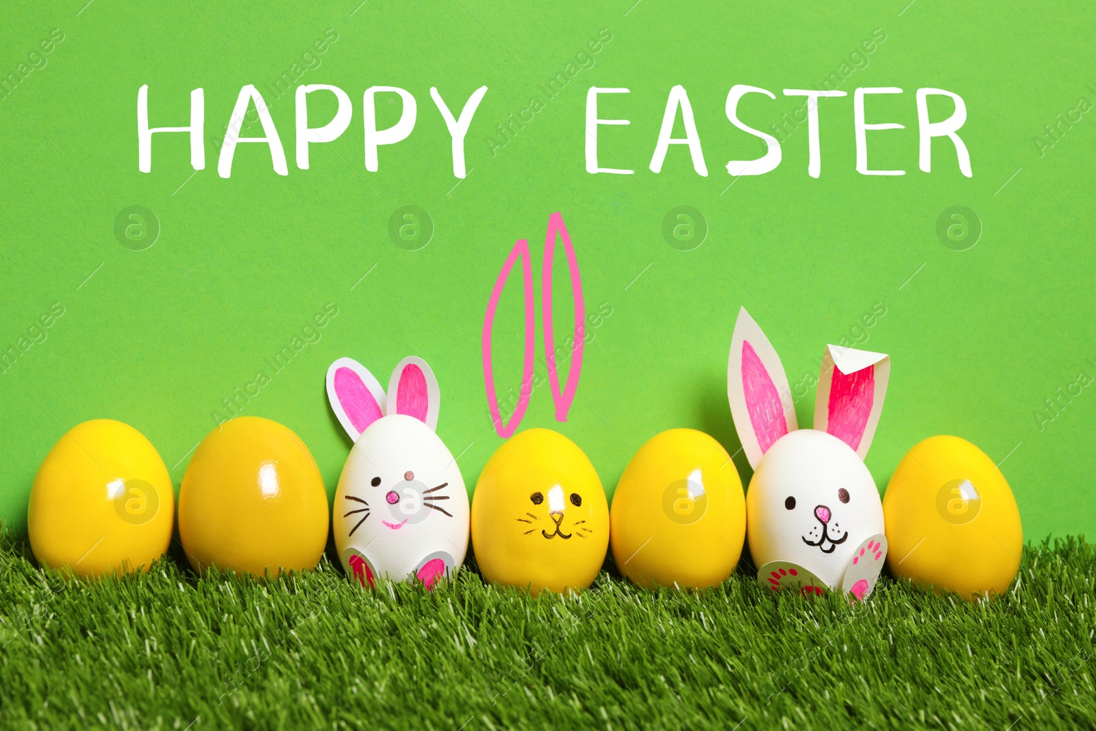 Image of White eggs with drawn faces and ears as Easter bunnies among others on green grass