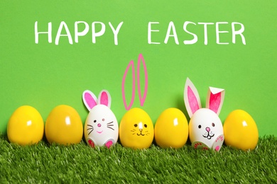 Image of White eggs with drawn faces and ears as Easter bunnies among others on green grass