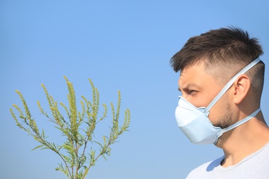 Man with ragweed branch suffering from allergy outdoors on sunny day