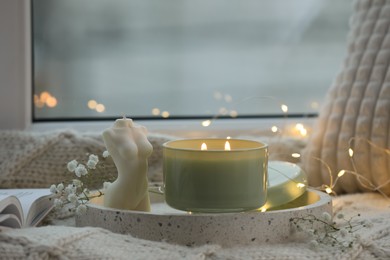 Beautiful burning candles, gypsophila and knitted blanket on window sill
