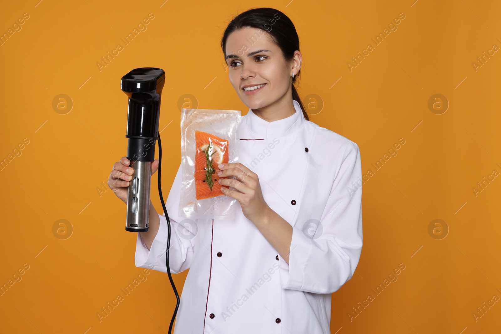 Photo of Chef holding sous vide cooker and salmon in vacuum pack on orange background