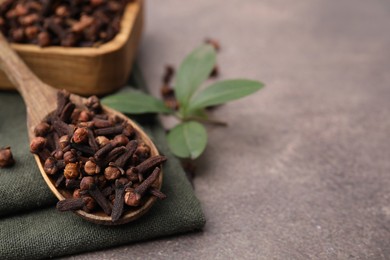 Photo of Wooden spoon with aromatic cloves and green leaves on brown table, closeup. Space for text