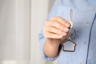 Woman holding house key with trinket, closeup. Space for text