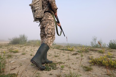 Photo of Man wearing camouflage with hunting rifle and backpack outdoors, closeup. Space for text