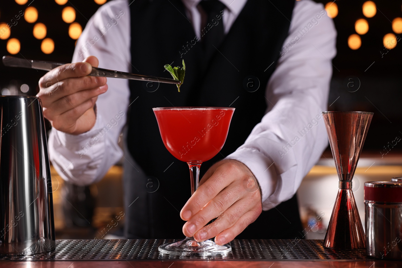 Photo of Bartender preparing fresh Martini cocktail in glass at bar counter, closeup