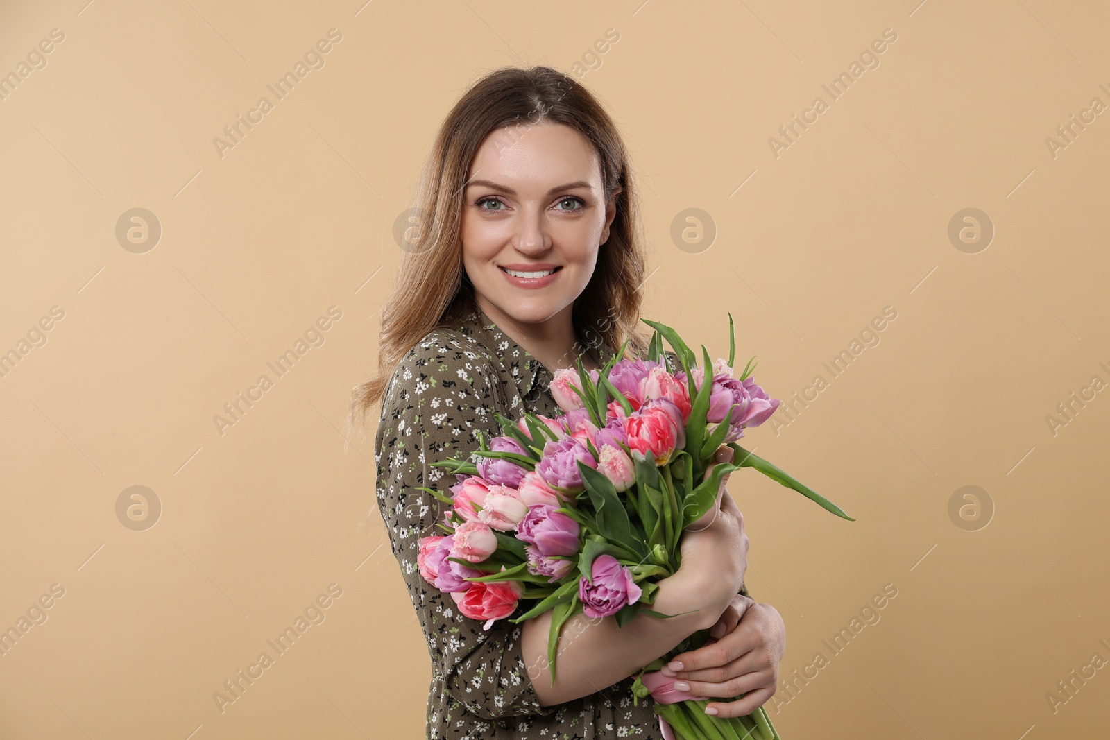 Photo of Happy young woman holding bouquet of beautiful tulips on beige background