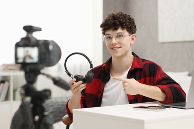 Smiling teenage blogger pointing at his headphones while streaming at home