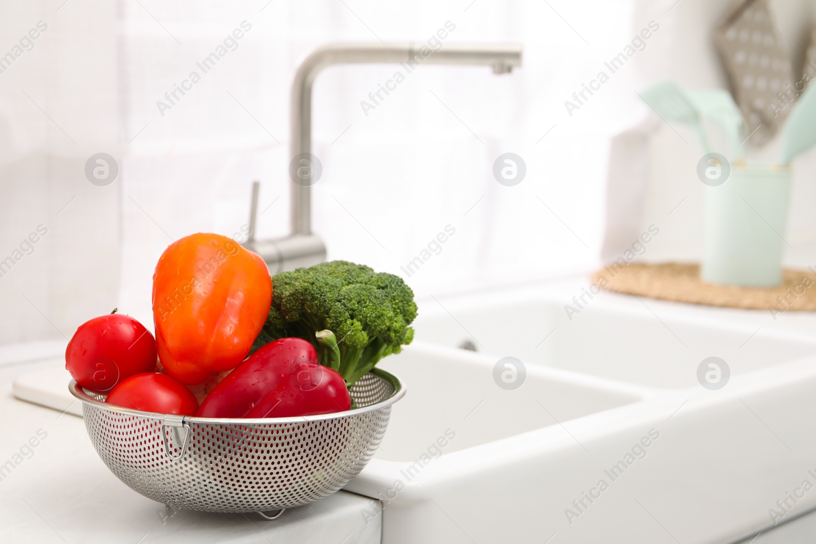 Photo of Fresh clean vegetables in colander on countertop near sink. Space for text