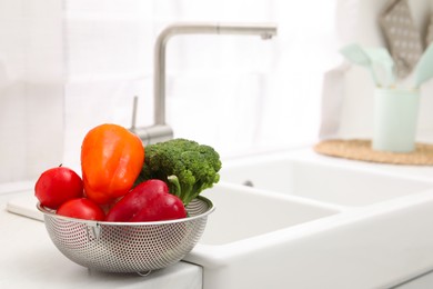 Photo of Fresh clean vegetables in colander on countertop near sink. Space for text