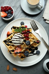 Photo of Delicious Belgian waffles with ice cream, berries and chocolate sauce served on grey textured table, flat lay