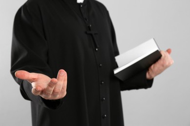 Priest with Bible praying on grey background, closeup