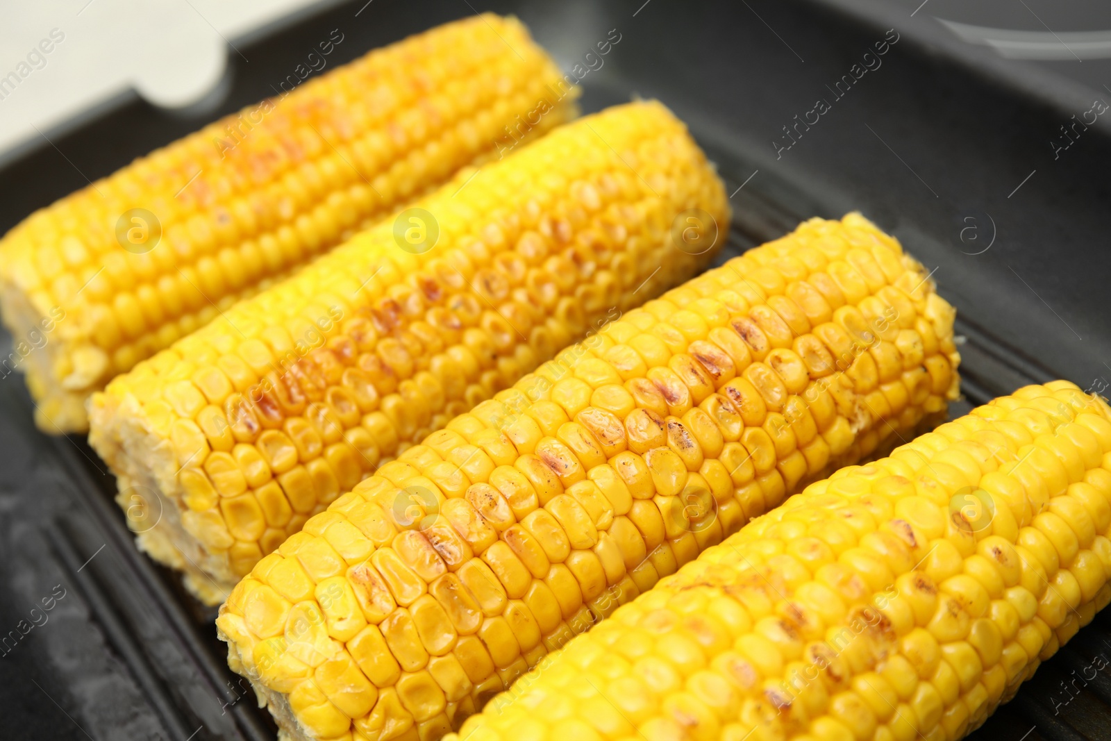 Photo of Fresh corn cobs on grill pan, closeup