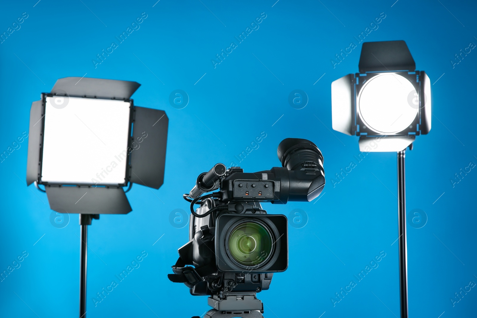 Photo of Professional video camera and lighting equipment on blue background