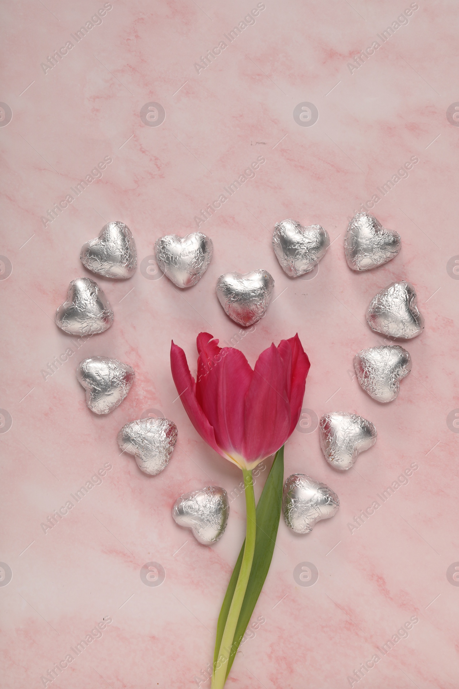 Photo of Heart made with delicious chocolate candies and beautiful tulip on pink table, flat lay