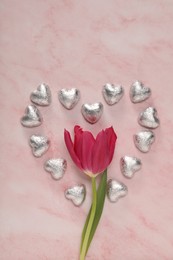 Photo of Heart made with delicious chocolate candies and beautiful tulip on pink table, flat lay