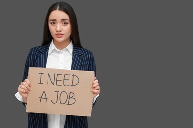 Photo of Young unemployed woman holding sign with phrase I Need A Job on black background, space for text