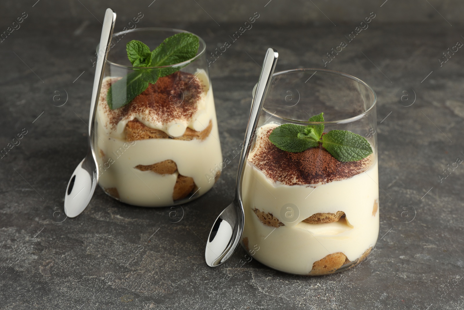 Photo of Delicious tiramisu with mint in glasses on grey table