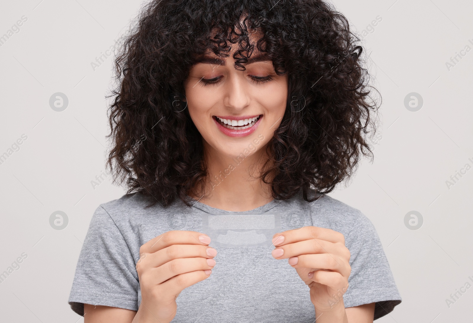 Photo of Young woman holding teeth whitening strips on light grey background