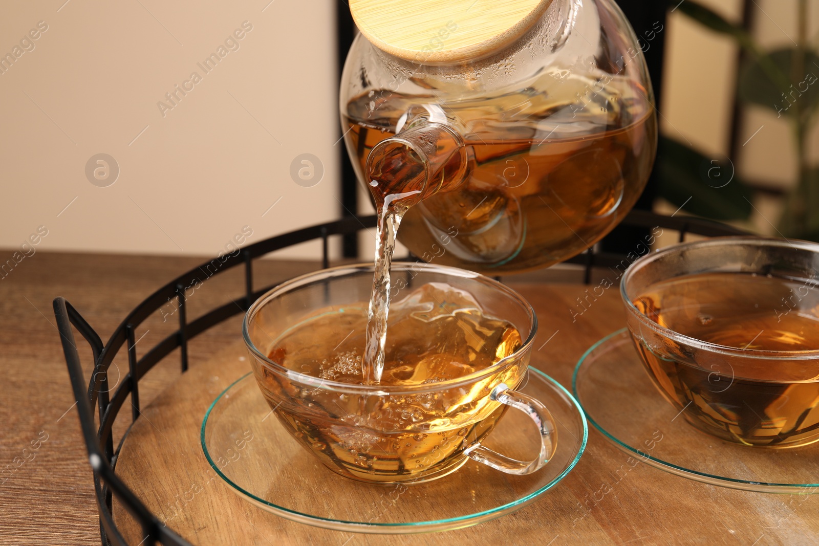 Photo of Pouring tasty tea into glass cup at wooden table, closeup