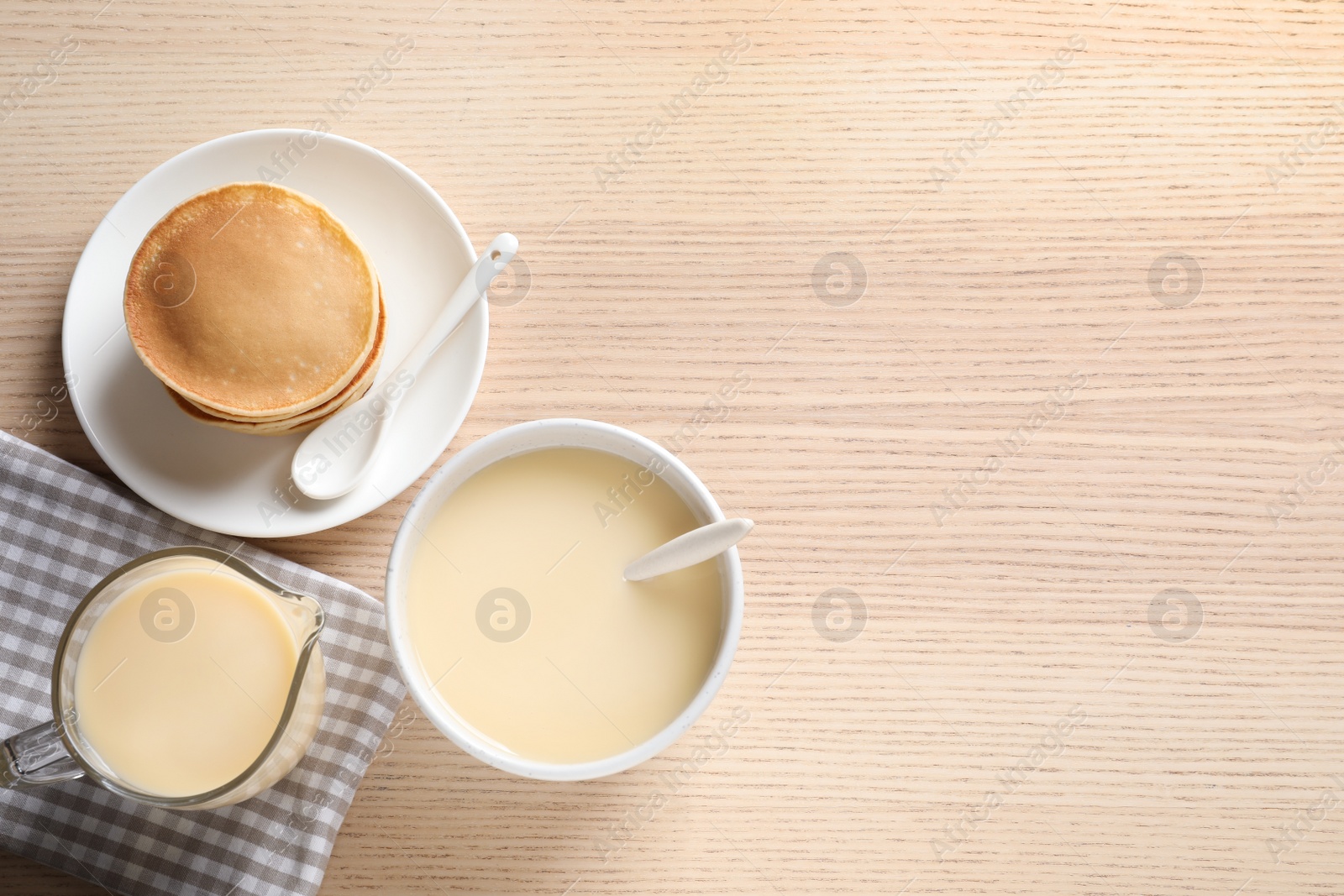 Photo of Bowl of condensed milk and pancakes served on wooden table, top view with space for text. Dairy products