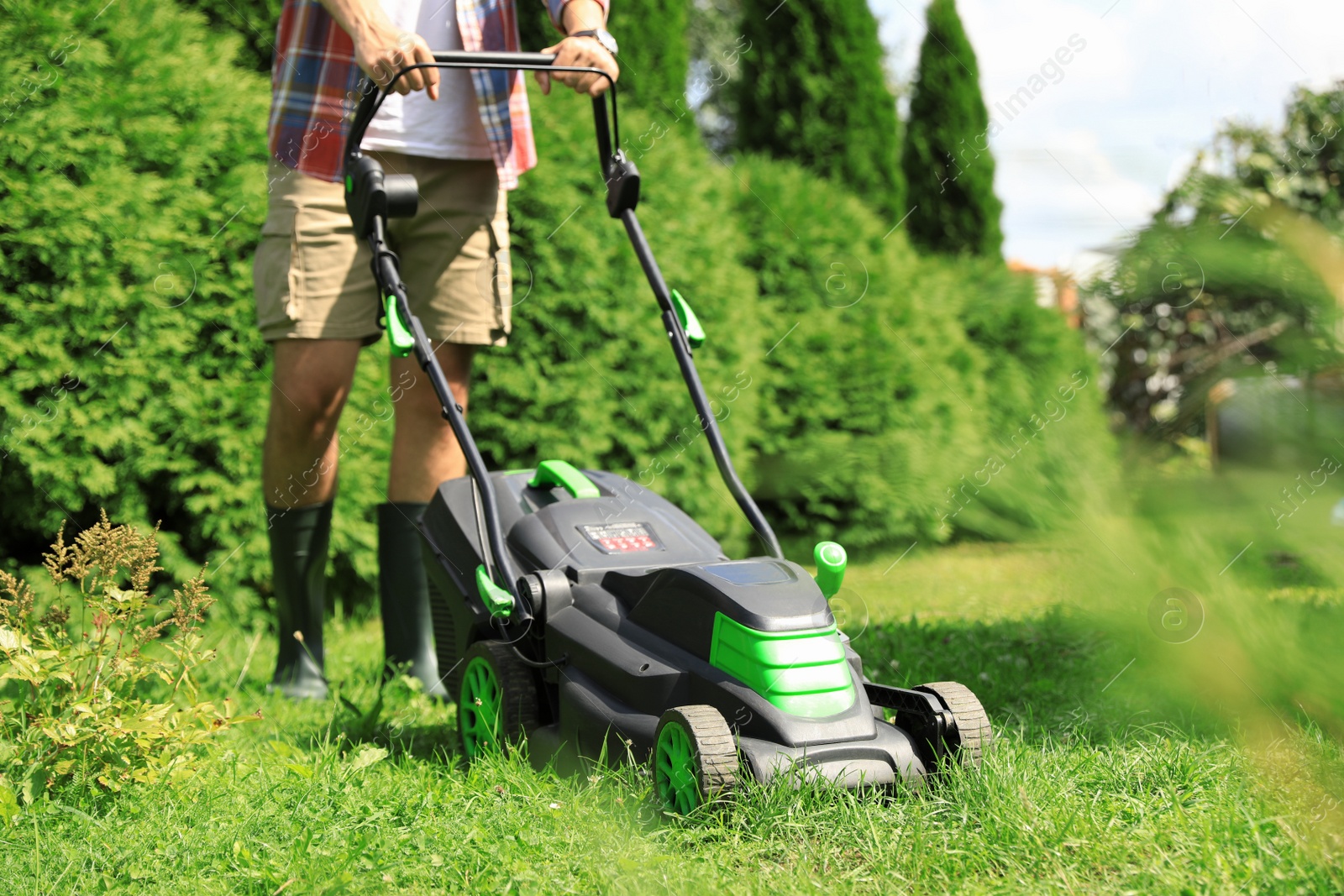 Photo of Man cutting grass with lawn mower in garden on sunny day, closeup