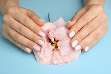 Woman with white nail polish touching pink eustoma flower on light blue background, closeup