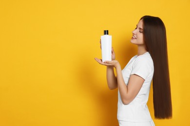Photo of Beautiful young woman holding bottle of shampoo on yellow background. Space for text