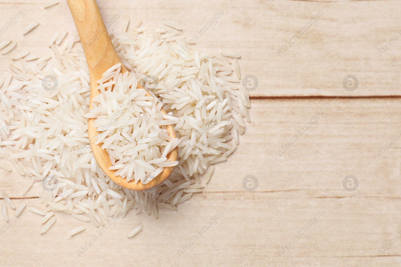 Photo of Raw basmati rice and spoon on white wooden table, top view. Space for text