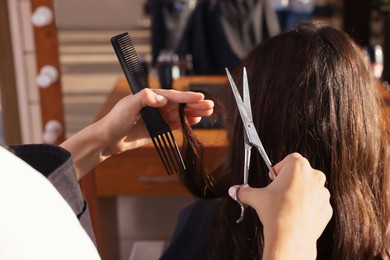 Photo of Professional hairdresser cutting woman's hair in beauty salon, closeup