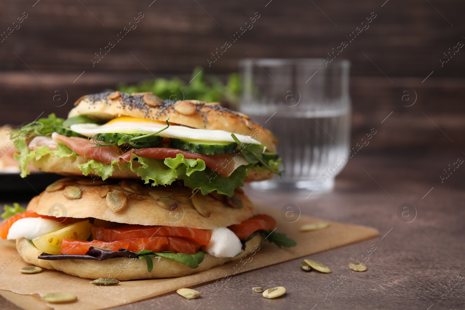 Photo of Stacked tasty bagel sandwiches on brown table, closeup. Space for text