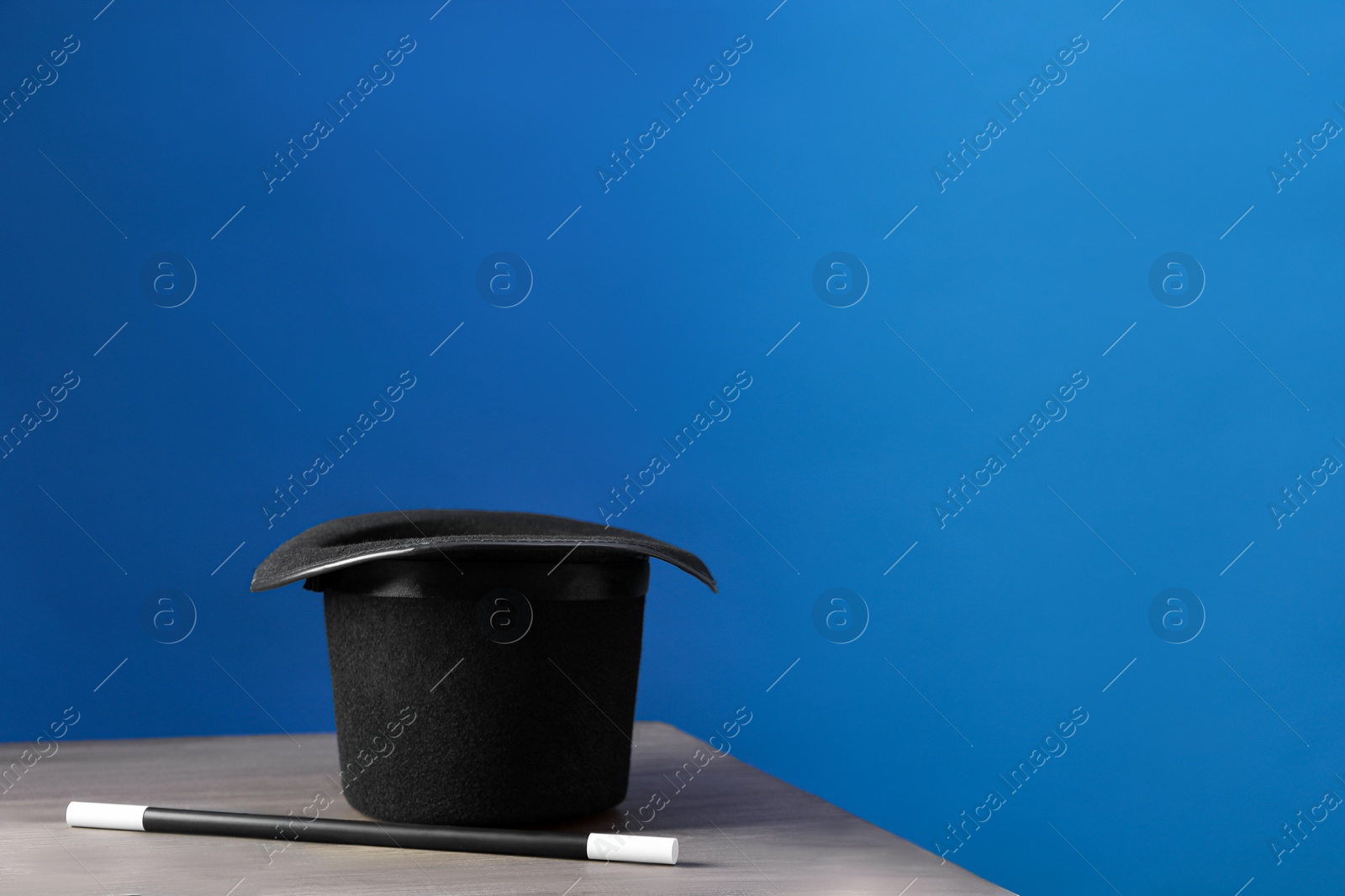 Photo of Magician's hat and wand on wooden table against blue background, space for text