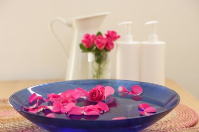 Photo of Pink roses and petals in bowl with water on table, closeup. Space for text