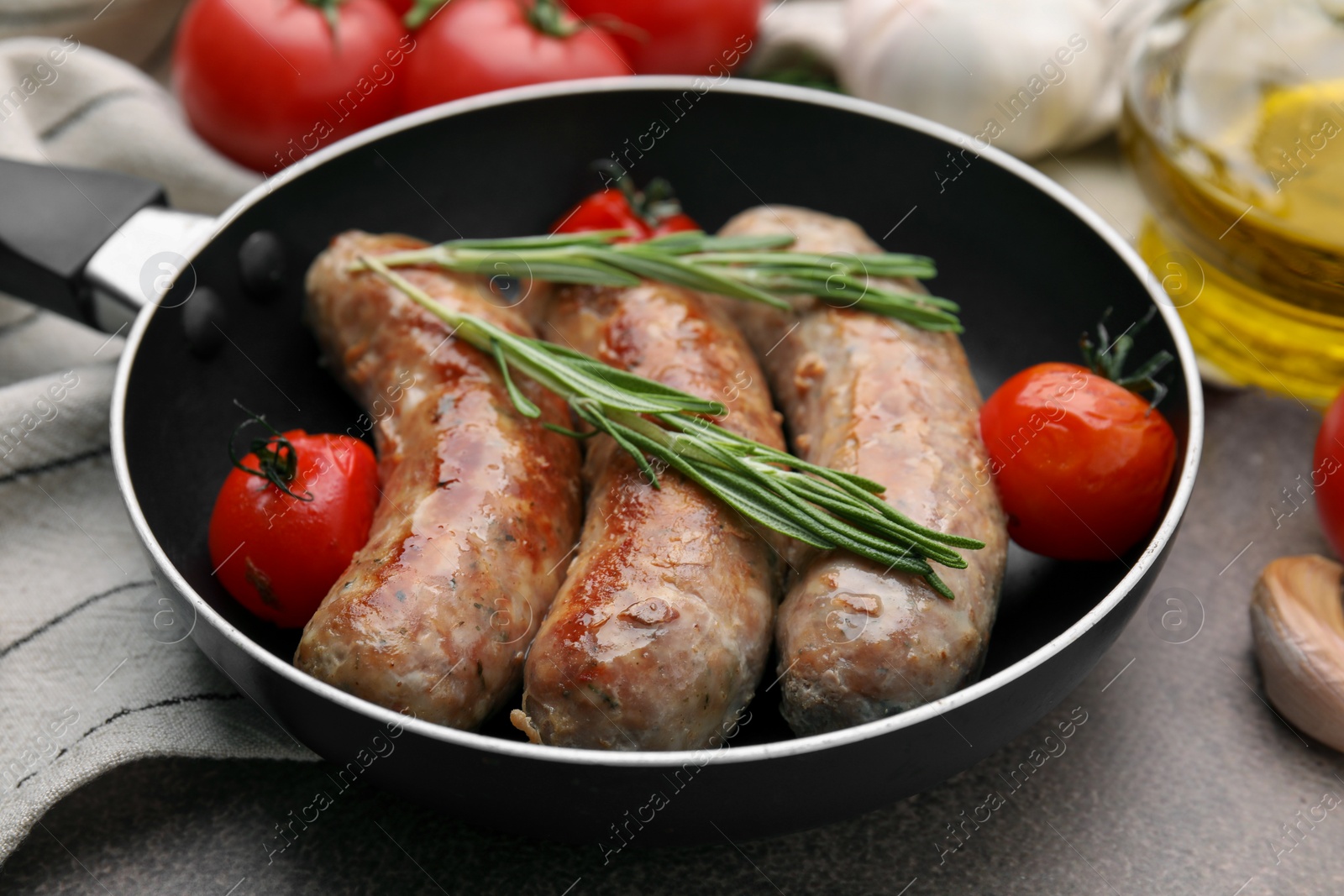 Photo of Frying pan with tasty homemade sausages, rosemary and tomatoes on brown table, closeup