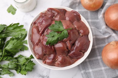 Photo of Bowl of raw chicken liver with parsley on white table, flat lay