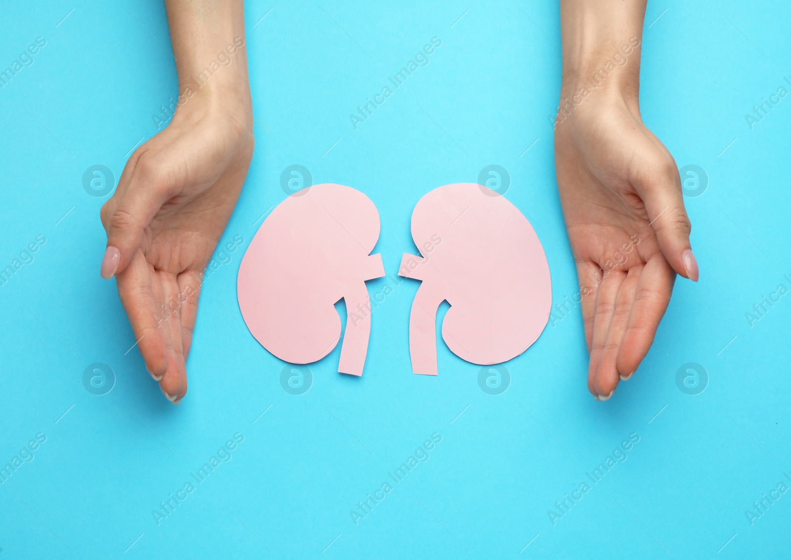 Photo of Woman protecting paper cutout of kidneys on light blue background, top view