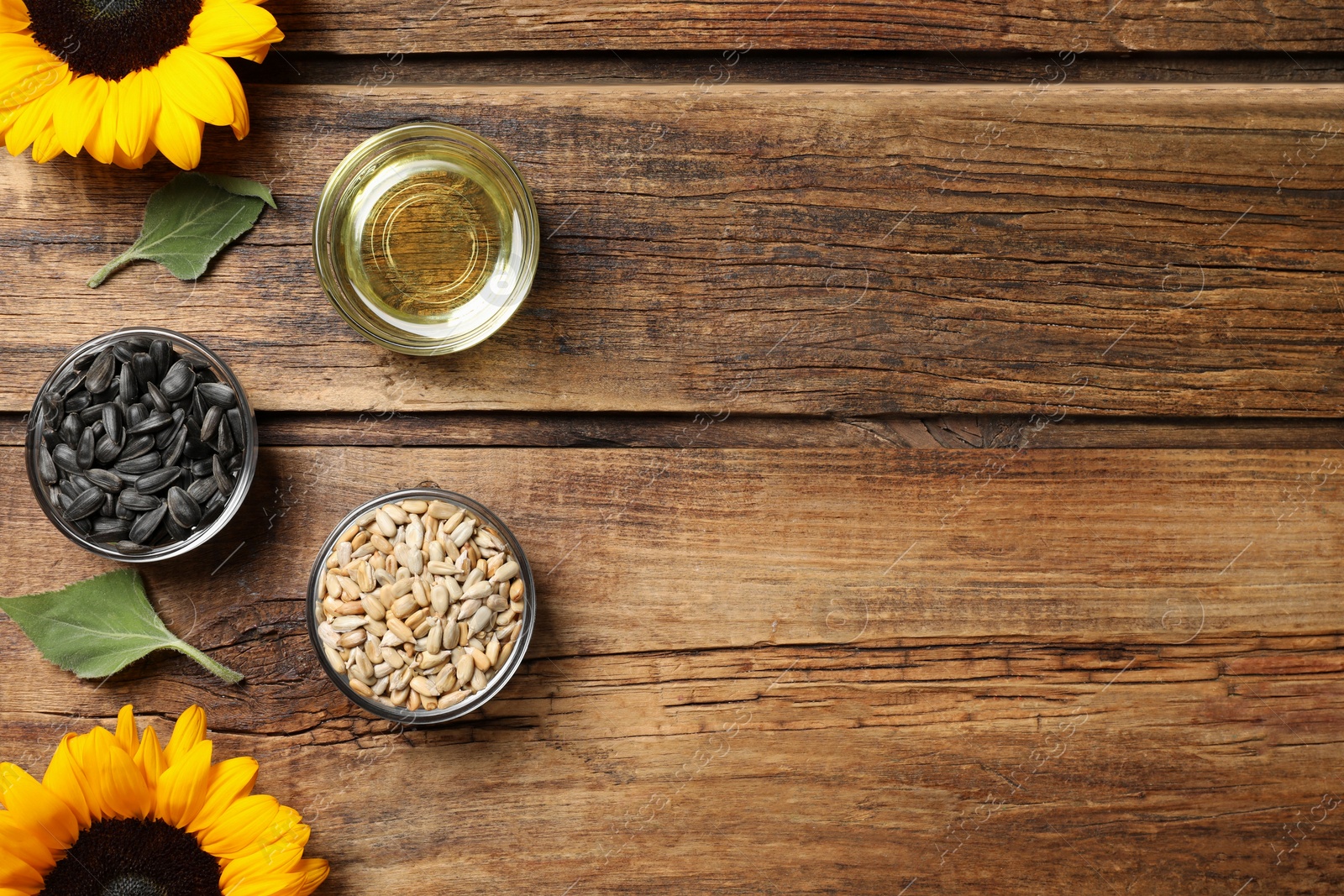 Photo of Bowls with sunflower cooking oil and seeds near flowers on wooden table, flat lay. Space for text