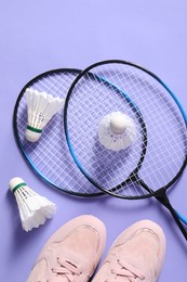 Feather badminton shuttlecocks, rackets and sneakers on violet background, flat lay