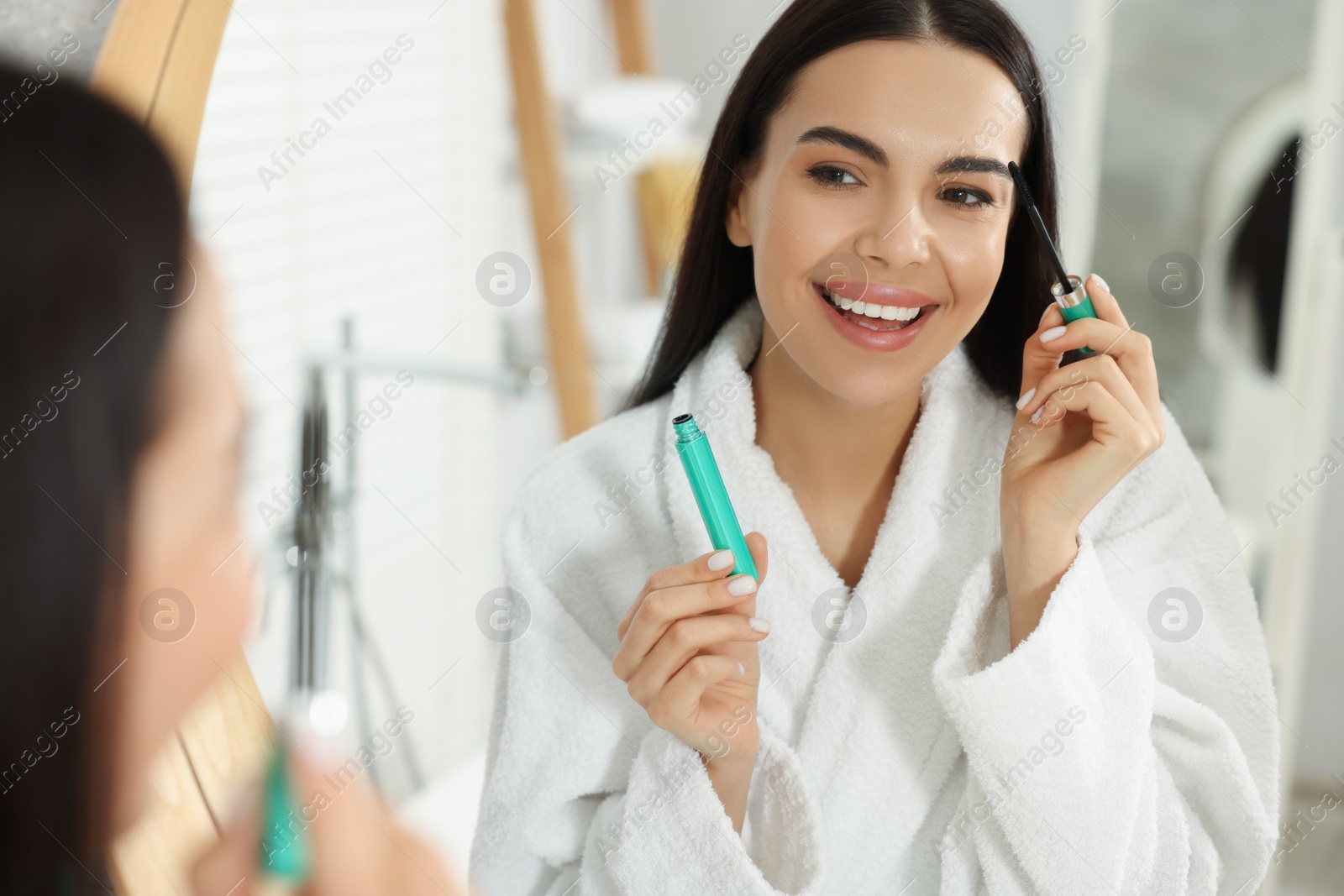 Photo of Beautiful young woman applying mascara near mirror in bathroom