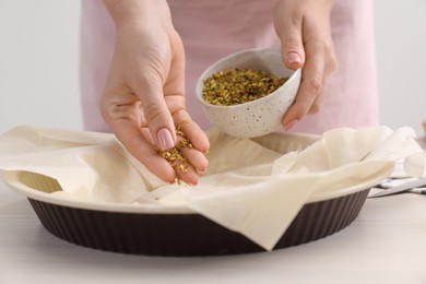 Photo of Woman putting filling into baking dish with dough to prepare baklava at white wooden table, closeup
