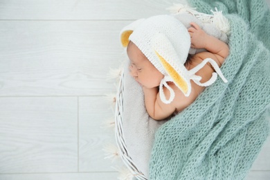 Photo of Adorable newborn child wearing bunny ears hat in baby nest, top view. Space for text
