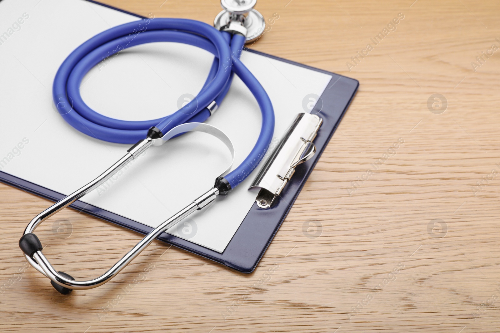 Photo of Clipboard with stethoscope on wooden table, closeup. Space for text