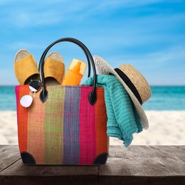 Image of Stylish bag with beach accessories on wooden surface near seashore 