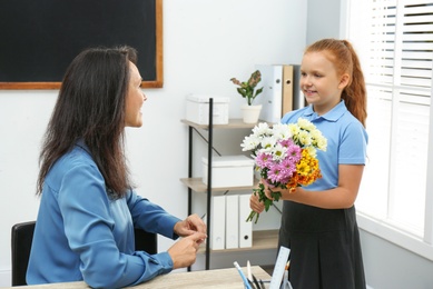 Photo of Schoolgirl with bouquet congratulating her pedagogue in classroom. Teacher's day