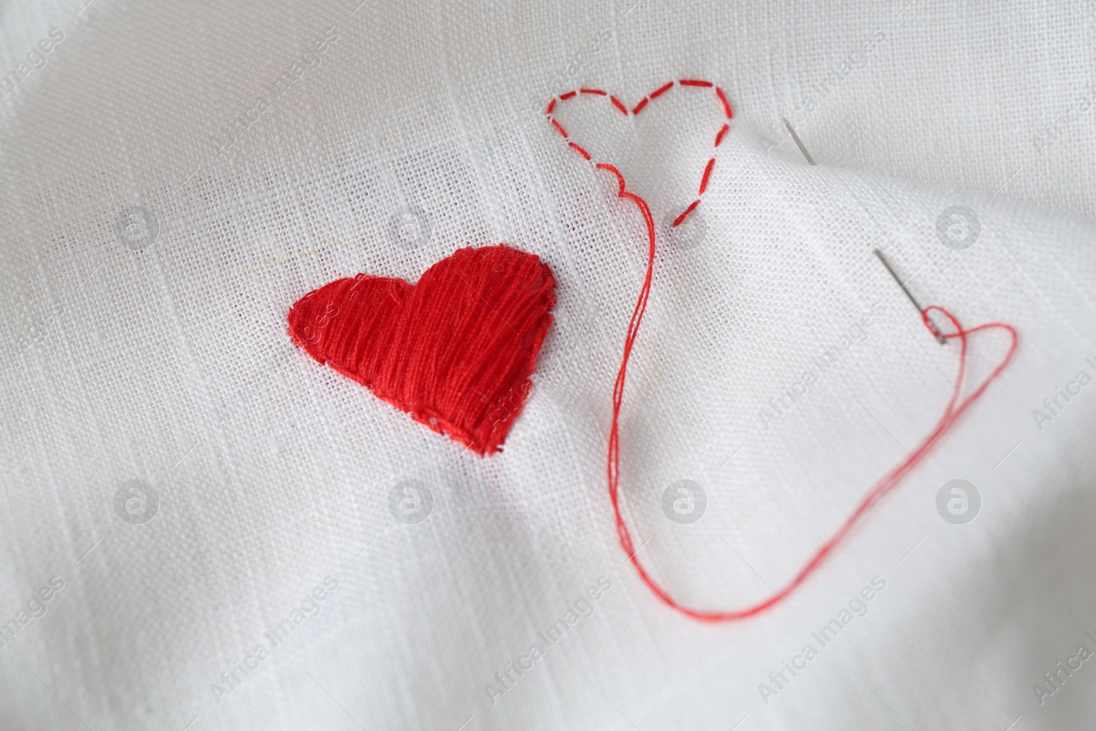 Photo of Embroidered red hearts and needle on white cloth, closeup