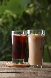 Photo of Glasses of fresh iced coffee on wooden table outdoors