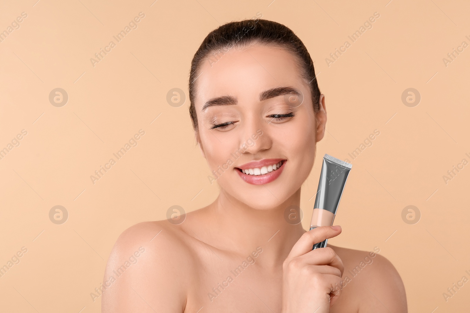 Photo of Woman holding tube of foundation on beige background