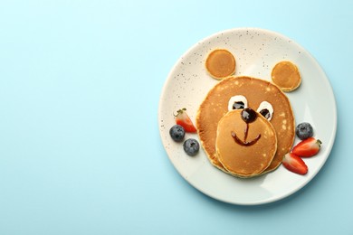 Creative serving for kids. Plate with cute bear made of pancakes and berries on light blue table, top view. Space for text